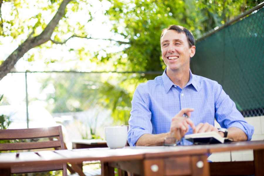 Shannon Pilcher smiles as he writes in his journal under a tree