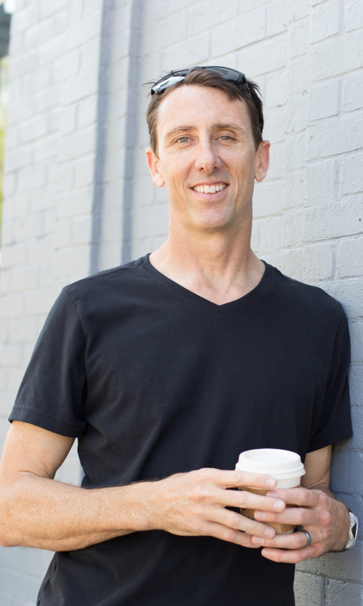 Shannon Pilcher leans against gray-colored brick building with coffee cup